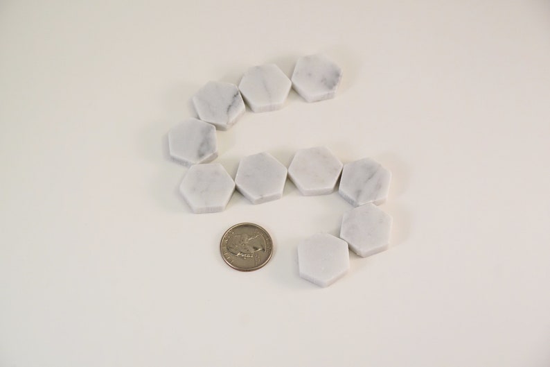 May include: A set of white marble hexagon tiles arranged in a curved pattern. A US quarter is included for scale.