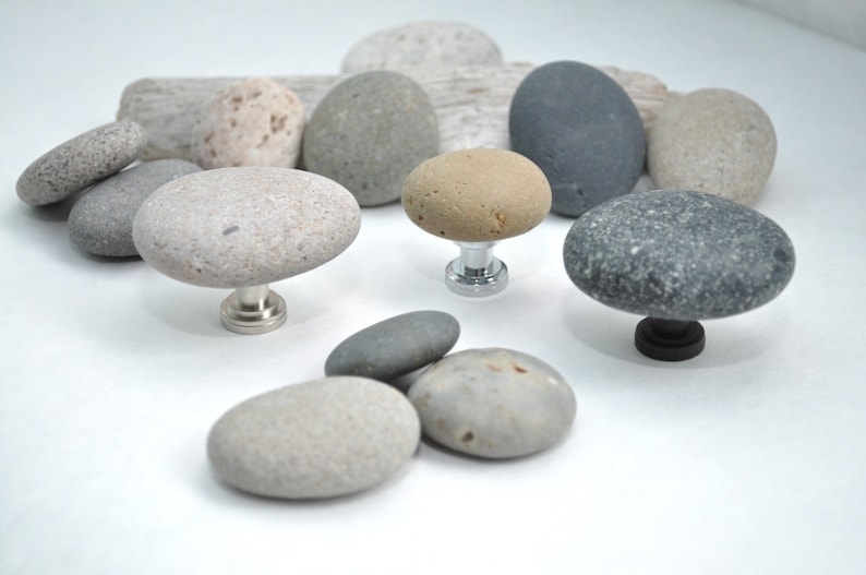 Peut inclure: Assortiment de galets de rivi&egrave;re lisses, gris, bruns et beiges avec une surface textur&eacute;e naturelle. Certains galets sont mont&eacute;s sur des bases m&eacute;talliques, cr&eacute;ant des boutons de cabinet uniques.