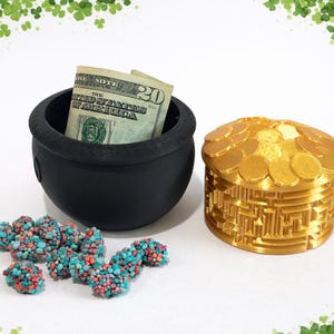 May include: A black pot with a twenty-dollar bill inside, a gold coin box, and colorful candy. The coin box is round with a maze-like design. The candy is blue, red, and white. The image has a St. Patrick's Day theme.