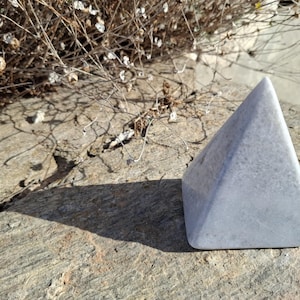 Peut inclure: Un cristal blanc, lisse, en forme de pyramide sur une surface grise texturée.