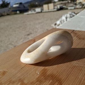 Può includere: Una scultura astratta bianca e liscia con un foro al centro. La scultura è in marmo e ha un colore leggermente avorio.