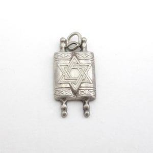 May include: A silver-colored pendant shaped like a Torah scroll. The pendant features a Star of David in the center and decorative scroll details. The pendant has a loop at the top for attaching to a chain.