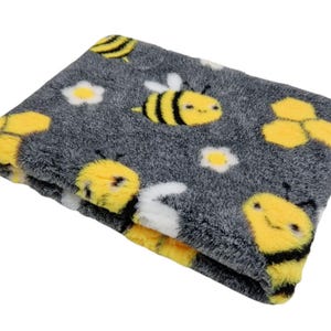 May include: A grey and yellow pet bed with a bee and honeycomb pattern. The bed is made of soft, plush fabric.