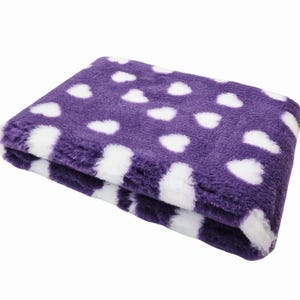 May include: Folded purple blanket with white heart-shaped polka dots. The blanket is made of a soft, plush material. The blanket is folded in half, showing the pattern on the top and the edge.