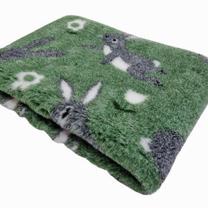 May include: A soft green plush blanket with a white and grey bunny rabbit pattern. The blanket is folded and has a fuzzy texture.