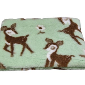 May include: A folded blanket with a light green background and a repeating pattern of brown deer and white flowers. The blanket is made of a soft, plush material, ideal for comfort.