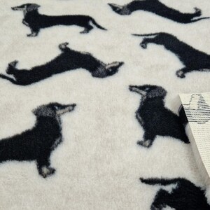 May include: White fabric with a repeating pattern of black dachshund dogs. The fabric has a soft, fuzzy texture.