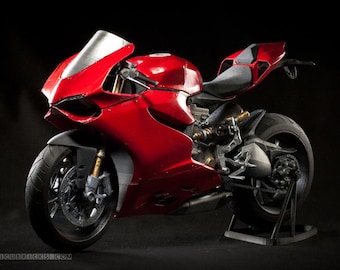 May include: A detailed model of a red sport motorcycle with a silver windshield. The motorcycle has black tires and a black seat. The model is displayed on a black stand against a black background. The motorcycle's body is a glossy red.