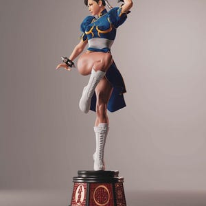 Puede incluir: Figura detallada de un personaje en pose dinámica, con un vestido azul con detalles dorados, botas blancas y pulseras negras. La figura está montada sobre una base decorativa con detalles rojos y dorados, mostrando un tema de artes marciales.