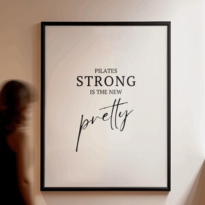 Może przedstawiać: Czarny plakat w ramie z białym tłem i tekstem "Pilates Strong is the new pretty" w kolorze czarnym.