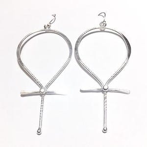 Könnte beinhalten: Ein Paar silberne Ankh-Ohrringe mit einem strukturierten Design. Die Ohrringe haben die Form des Ankh-Symbols, einem alten ägyptischen Hieroglyphen, das das Leben darstellt.