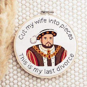 Peut inclure: Un cerceau de broderie blanc avec un motif de point de croix représentant un portrait de dessin animé du roi Henri VIII. Le texte autour du portrait dit "Cut my wife into pieces this is my last divorce."