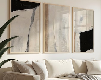May include: Three framed abstract art pieces with neutral tones hang above a cream-colored sofa. The artwork features black and white brushstrokes. A gray throw blanket and pillows adorn the sofa. A potted plant is on the left, and another plant is near the window.
