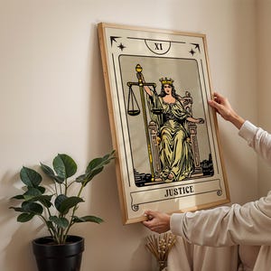 May include: A framed tarot card print featuring the Justice card. The artwork depicts a robed figure holding scales and a sword, with the word "JUSTICE" at the bottom. The frame is light-colored wood.