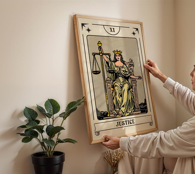 May include: A framed tarot card print featuring the Justice card. The artwork depicts a robed figure holding scales and a sword, with the word "JUSTICE" at the bottom. The frame is light-colored wood.