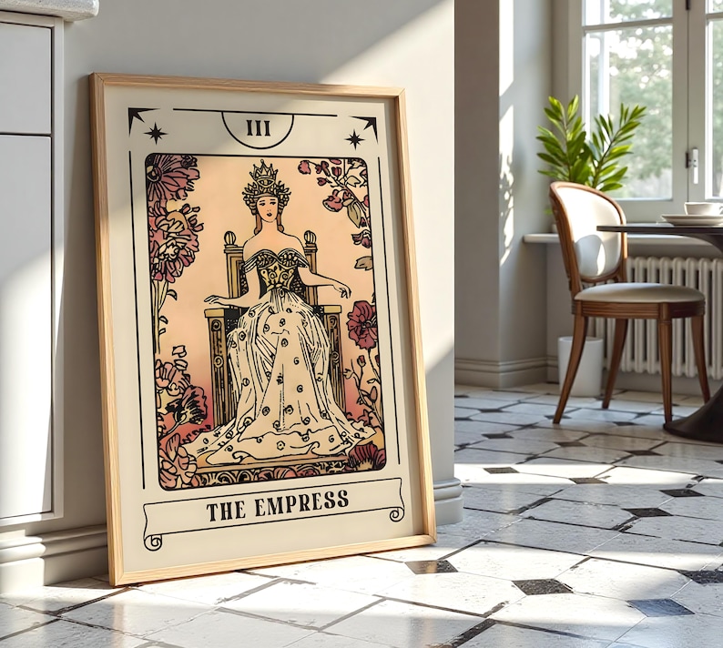 May include: A framed print of The Empress tarot card. The artwork features a woman in a gown and crown seated on a throne, surrounded by floral elements. The color palette includes beige, pink, and black, with the title "THE EMPRESS" at the bottom.