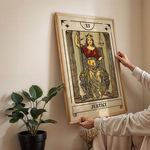 K&ouml;nnte beinhalten: Ein gerahmter Wandkunstdruck, der die Tarotkarte Gerechtigkeit mit der Beschriftung XI zeigt. Die Illustration stellt eine gekr&ouml;nte Figur dar, die zwischen zwei S&auml;ulen sitzt, ein Schwert in der einen und eine Waage in der anderen Hand h&auml;lt.