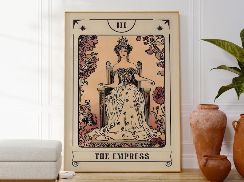 May include: A framed tarot card print featuring "The Empress." The artwork depicts a woman in a crown and gown seated on a throne, surrounded by floral elements. The color palette includes beige, pink, and black, with the title at the bottom.