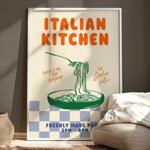 May include: A white framed poster with an orange and green illustration of a plate of pasta with the text "ITALIAN KITCHEN" in orange and green. The text "Pasta is my love language" and "La Dolce Vita" are written in cursive on the poster. The poster also includes the text "FRESHLY MADE PASTA 3PM-9PM".