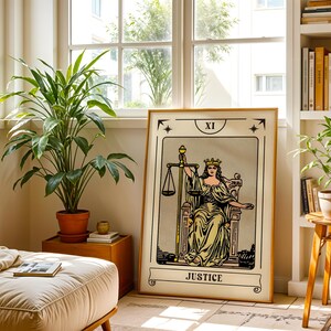 May include: A framed Justice tarot card print with a gold frame. The artwork features a woman holding scales, with the word "JUSTICE" at the bottom. The print is displayed in a well-lit room with plants and a window.