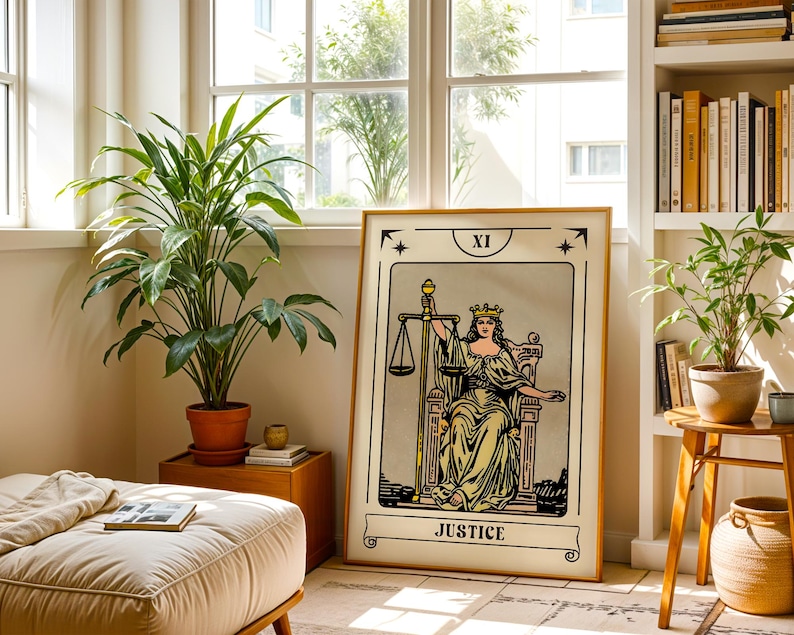 May include: A framed Justice tarot card print with a gold frame. The artwork features a woman holding scales, with the word "JUSTICE" at the bottom. The print is displayed in a well-lit room with plants and a window.