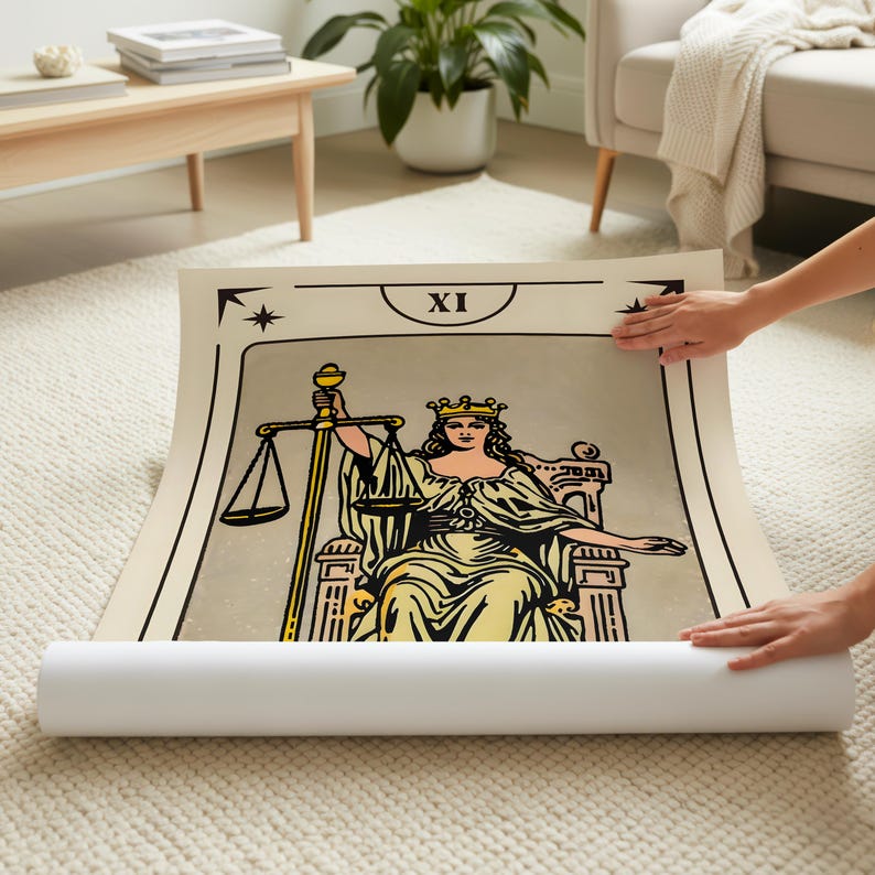 May include: A rolled-up tarot card print featuring the Justice card. The illustration depicts a woman with a crown, holding scales and a sword. The card has a beige background with black and gold accents, and the Roman numeral XI.