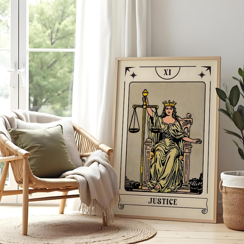 May include: A framed tarot card print featuring the Justice card. The artwork depicts a robed figure holding scales, with the word "JUSTICE" at the bottom. The print is displayed next to a wicker chair with a green pillow and a beige blanket.