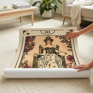 May include: A rolled-up tarot card print featuring a seated woman wearing a crown and ornate gown. The card is bordered in black with floral accents and the Roman numeral III at the top. The print is on a cream-colored background.