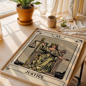 May include: A framed tarot card print of the Justice card, featuring a seated woman holding scales and a sword. The card has a beige background with black and yellow illustrations. The word "JUSTICE" is printed at the bottom.