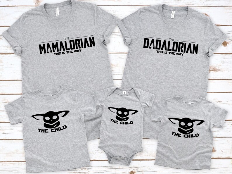 May include: A family set of gray t-shirts and a onesie. Two adult shirts read "The Mamalorian" and "The Dadalorian", with "This is the Way" below. The other shirts and onesie say "The Child" with a black graphic.
