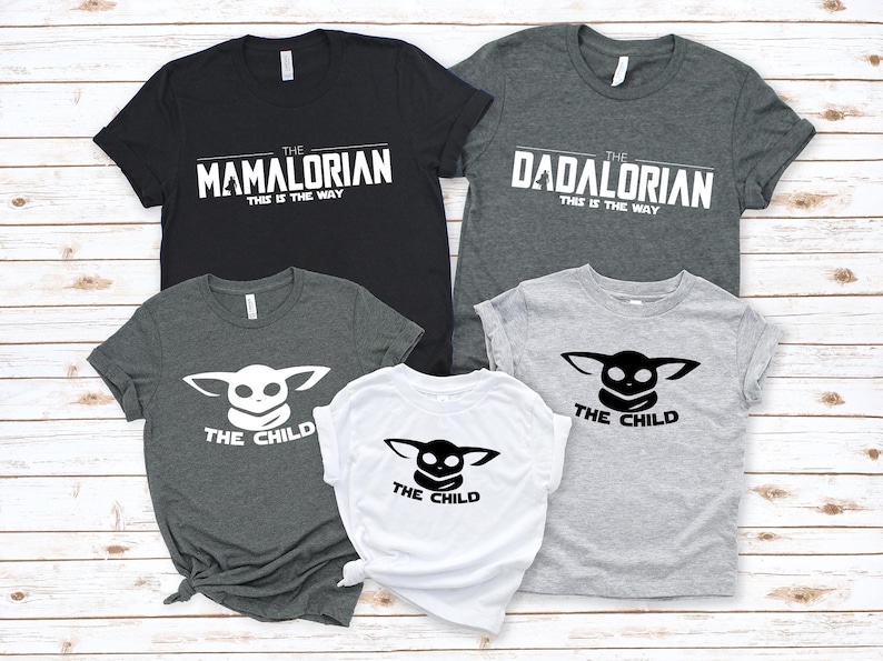 May include: A collection of five t-shirts with white text on various colors. The shirts feature the phrases "The Mamalorian", "The Dadalorian", and "The Child". The text "This is the Way" is below "The Mamalorian" and "The Dadalorian".