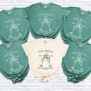 Pu&ograve; includere: Una collezione di magliette verdi e color crema. Le magliette verdi dicono "The Bach Club" con calici di champagne e il testo "Rachel's Bachelorette Florida". La maglietta color crema dice "The Bride".