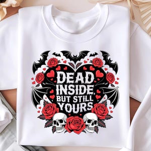 Puede incluir: Sudadera blanca con un diseño gráfico en negro y rojo. El gráfico presenta un corazón con murciélagos, rosas y calaveras. El texto dice "Dead Inside, But Still Yours."