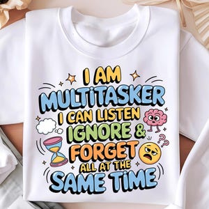 Puede incluir: Sudadera blanca con un gráfico colorido que dice "Soy un multitarea Puedo escuchar ignorar y olvidar todo al mismo tiempo". El gráfico incluye un cerebro, un reloj y una cara sonriente.