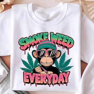 May include: White sweatshirt with a graphic of a monkey wearing sunglasses and a hat, holding a joint. The text "SMOKE WEED EVERYDAY" is written in dripping pink and green letters.