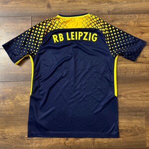 May include: A navy blue soccer jersey with yellow accents and the text "RB LEIPZIG" on the back.