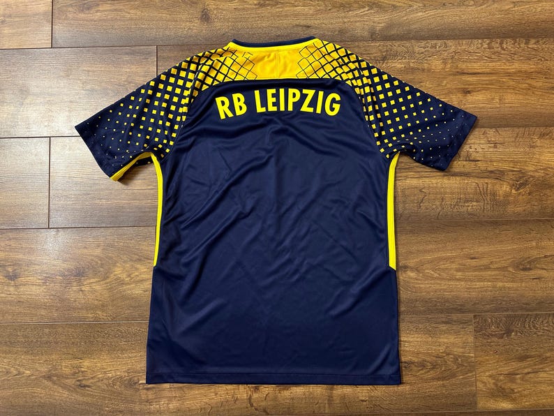 May include: A navy blue soccer jersey with yellow accents and the text "RB LEIPZIG" on the back.