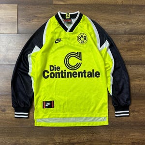 May include: A yellow long-sleeve soccer jersey with black and white trim. The jersey has the Nike logo, the Borussia Dortmund logo, and the text "Die Continentale".