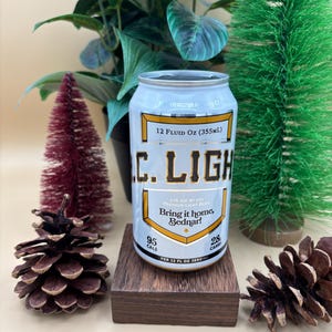 May include: A silver can of C. Light Premium Light Beer with the text "Bring it home, Bednar!" and the nutritional information 95 calories and 28 carbs per 12 fluid ounces. The can is sitting on a wooden coaster.