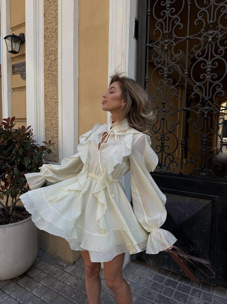 K&ouml;nnte beinhalten: Eine wei&szlig;e Keramik-Tasse mit schwarzem Henkel und dem Text "But First, Coffee" in fetter, schwarzer Schrift. Die Tasse steht vor einem verschwommenen Hintergrund, der eine gem&uuml;tliche Umgebung andeutet.