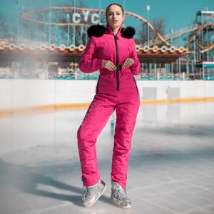 May include: A bright pink snowsuit with a black zipper and black fur trim around the collar. The snowsuit has a fitted waist and is worn with silver boots. The background includes a roller coaster and a blue sky.
