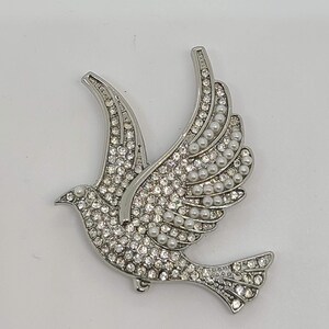 May include: A silver dove brooch with clear and white rhinestones. The dove is in flight with its wings spread.