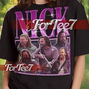 May include: Black unisex t-shirt featuring a graphic print of a group of men with the text "Nick For Tee7" in pink. The shirt is being modelled by a person in a woodland setting.