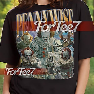 Puede incluir: Camiseta unisex negra con un estampado gráfico de Pennywise de la película "IT" y el texto "Pennywise For Tee7".