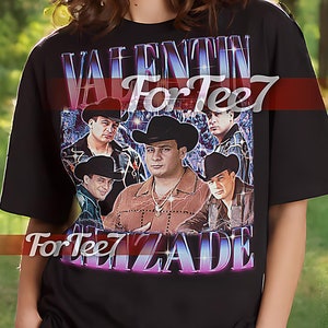 May include: Black unisex t-shirt featuring a graphic of a man in a cowboy hat with the text "VALENTIN ELIZADE" in a purple and pink font. The shirt also has the text "For Tee7" in a pink font. The shirt is being modeled.