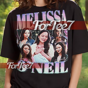 May include: Black unisex t-shirt featuring a graphic print of a woman's face and the text "MELISSA For Tee7 NEIL".