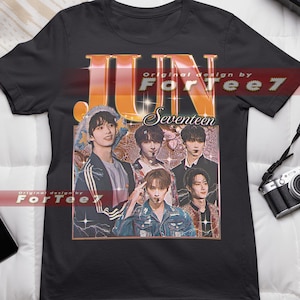 May include: Black t-shirt with a graphic of a K-pop group called Seventeen. The graphic is in a retro style with the word "JUN" in large, bold letters. The text "Original design by ForTee7" is also on the shirt.