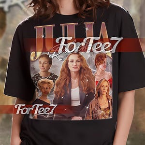 May include: Black unisex t-shirt featuring a graphic print of Julia Roberts from the film "Pretty Woman". The text "Julia For Tee7" is printed in gold lettering on the shirt.