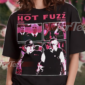 May include: Black unisex t-shirt featuring a graphic from the movie "Hot Fuzz". The design includes a collage of images from the film, with the title in pink text. The shirt also has the text "A Film Edgar Wright" and "2007".
