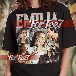 Könnte beinhalten: Schwarzes Unisex-T-Shirt mit einem grafischen Druck einer Gruppe von Personen aus der Fernsehserie "Emily in Paris". Der Text "For Tee7" ist auf dem Shirt aufgedruckt.